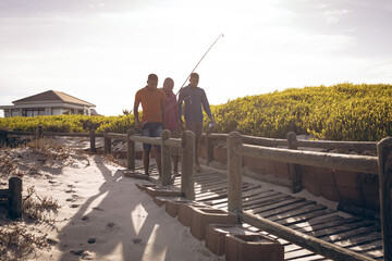 African american father and his two sons with fishing rods walking together on the bridge