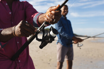 Mid section of african american father and his son with fishing rods fishing together at the beach