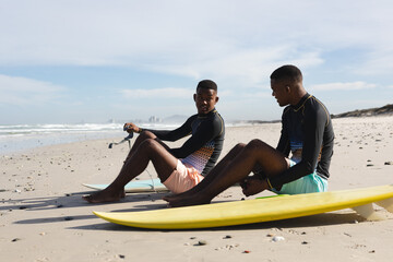 African american brothers with surfboards sitting at the beach
