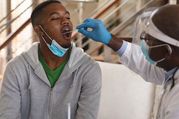 African american senior male doctor performing throat swab test on african american man at home