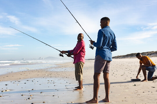 African american father and his two sons with fishing rods fishing together at the beach - Powered by Adobe