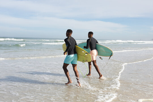African american brothers with surfboards running towards the waves at the beach