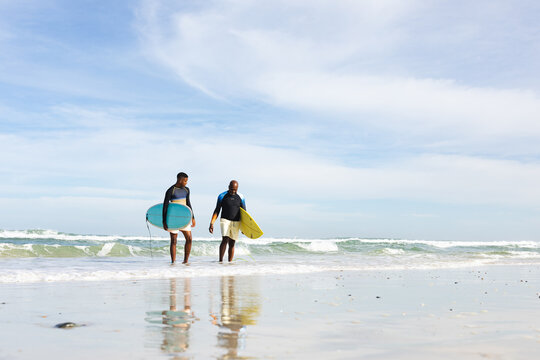 African american father and son with surfboards walking towards the beach