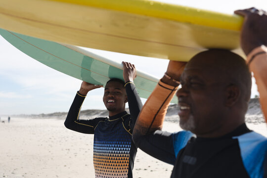 African american father and son carrying surfboards on their heads at the beach