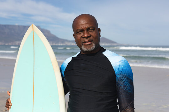 Portrait of african american senior man with surfboard standing at the beach
