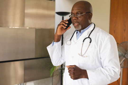 African american senior male doctor talking on smartphone at home