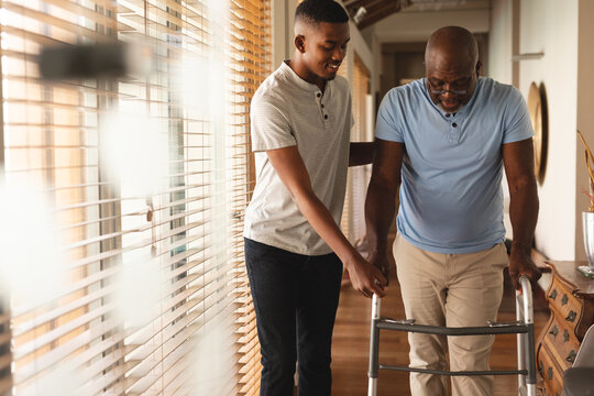 African american young man helping his father to walk with walking frame at home