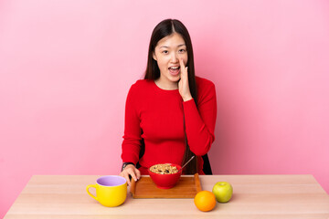 Young Chinese girl  having breakfast in a table shouting with mouth wide open