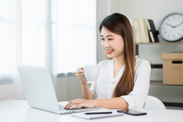 Young asian beautiful business woman working with laptop sitting at home drinking coffee. Smiling charming happy young female doing homework meeting conference with team at home.