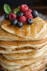 Close-up of pancakes with dripping honey and berries on black background