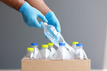 A young man wearing rubber gloves arranged plastic bottles into a carton. He assumes plastic bottles will sort of trash before throwing them into the bin.