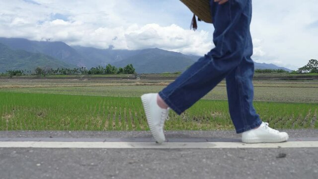 cropped image steps of a person walking with sneakers and jeans on the sunny country road at Mr. Brown Avenue with green paddies and mountains in the background