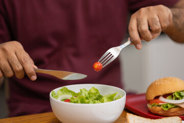 A young man eating breakfast. Breakfast set includes bread, bacon, salad and sausage.