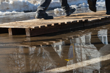 Male feet pass through a puddle on wooden pallets that are used to avoid getting their feet wet