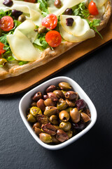 bowl of Taggiasca olives in the foreground, pizza on cutting board in the background