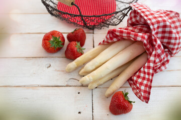 Fresh white asparagus and strawberries with basket on bright vintage wood. Seasonal food...