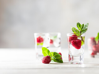 Raspberry vodka glass shot with fruit inside. Fresh summer shots for party. Berries in alcohol glass. Glass of sparkling water.