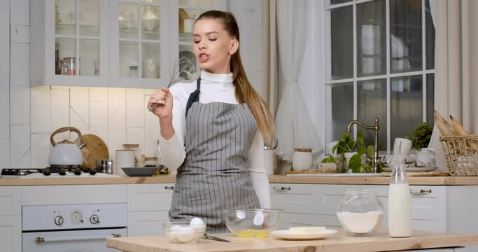 Happy cooking. Young lady chef singing into whisk, pretending be singer, preparing dough for pastry at home kitchen