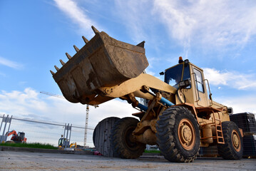 Wheel loader with a bucket at construction. Heavy machinery for loading and unloading works and road work. Public works, civil engineering, road construction. Tower crane in action. Crane on formwork