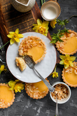 Lemon mini tarts in a plate on a wooden board on a gray table. Sweets and flowers. Bright yellow dessert.