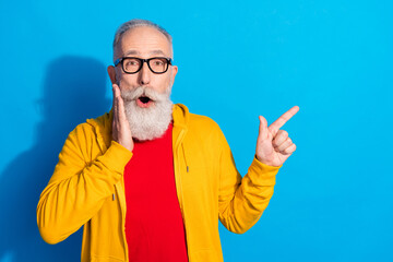 Photo of shocked surprised amazed mature man point finger copyspace advertise product isolated on blue color background