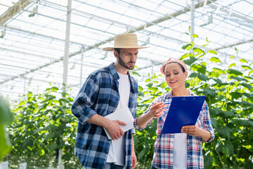 Obraz premium smiling african american farmer pointing at clipboard near colleague with digital tablet