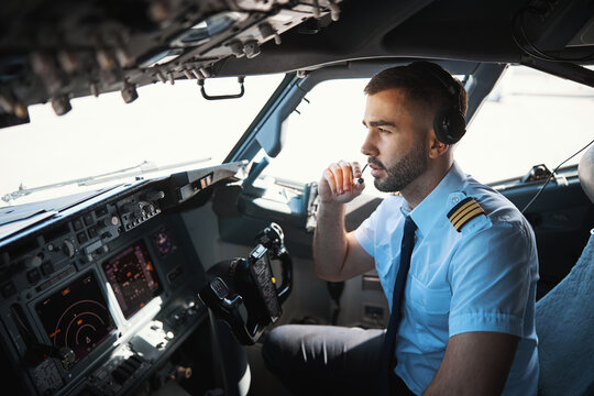 Serious pilot talking to the coworkers in the microphone