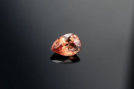 Natural mined drop faceted peach color sapphire loose gemstone setting for jewelry making. Clean, gentle classic heat treatment. Dark gray gradient background.