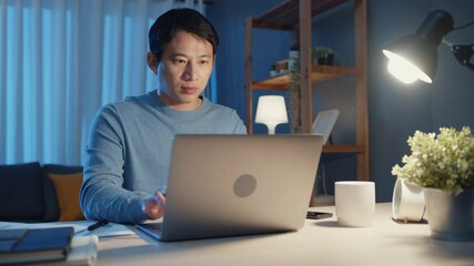 Asia freelance businessman focus working typing on laptop computer online remotely from company on desk in living room at home overtime at night, Work from home during COVID-19 pandemic concept. - Powered by Adobe