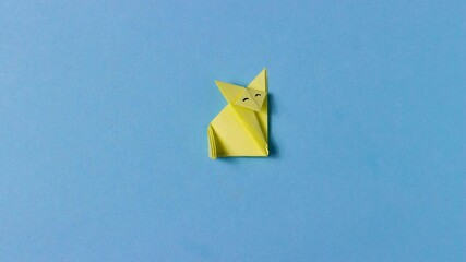Yellow origami fox folds from paper. On a blue background. Concept of love animals, pastime, hobbies, activities with children, symbol.
