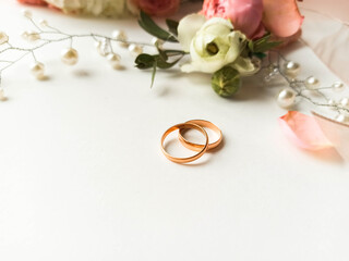 Pink flowers, pearl jewelry and two gold wedding rings on a white background. Wedding concept. Isolated	