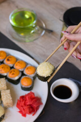 Woman holding sushi with chopsticks over plate of sushi