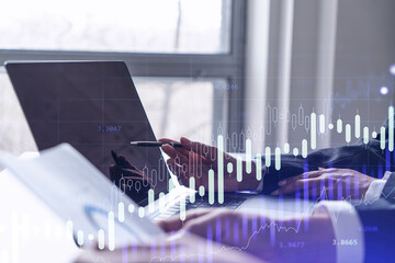 Two traders researching historic data to predict stock market behavior using laptop. Internet trading concept. Forex and financial hologram chart. Forecasting and planning.