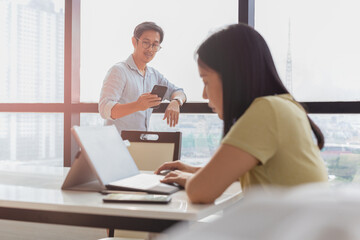 Obraz premium Businessman using cell phone with woman working on laptop in foreground.