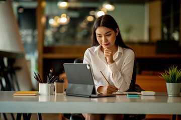 Portrait of Asian young female Businesswoman working on laptop computer doing finances,accounting analysis,report,data and pointing graph at the office.