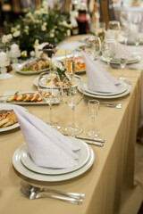 Close up of festive table setting with wine glasses, fresh flowers on beige tablecloth