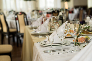 Close up of festive table setting with wine glasses, fresh flowers on beige tablecloth