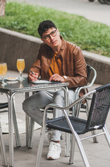 Young man in fashion spring clothes. On his weekend, relaxed in city having a beer and drawing  under trees, on a table terrace in the bar