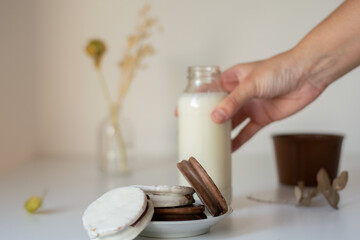 alfajores rellenos de dulce de leche cubiertos de chocolate con una botella de leche al lado, sobre una mesa blanca