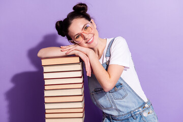 Portrait of pretty positive young girl hands head on book stack beaming smile isolated on purple color background