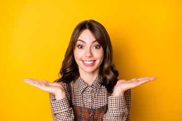 Photo portrait of girl keeping blank spaces on hands smiling isolated on bright yellow color background