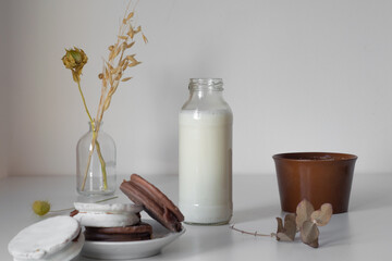vaso o botella de leche sobre una mesa de color blanco, acompañado de alfajores tradicionales de argentina de dulce de leche con chocolate