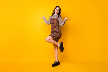 Fototapeta na wymiar Full length body size photo of smiling schoolgirl wearing uniform holding empty spaces on hands isolated vivid yellow color background