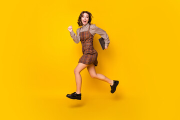 Fototapeta na wymiar Full size profile photo of optimistic funny brunette lady run with laptop wear shirt dress sneakers isolated on vivid yellow background
