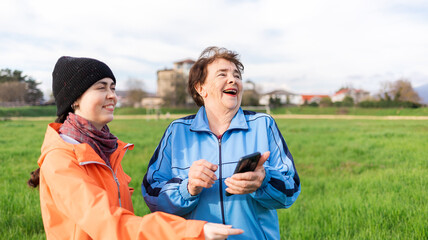 Portrait of a happy young and elderly women with a phone in her hand, looking away. Outdoor. International Day of Older Persons