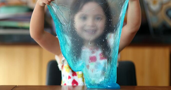Little girl playing with slimy plasticine creating a bubble with blue slime