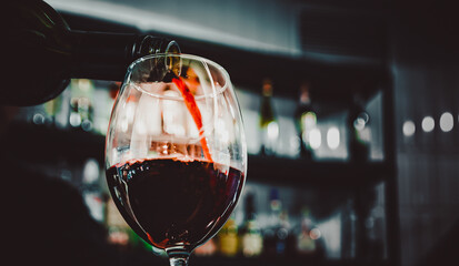 bartender pouring red wine into a glass in cafe or bar
