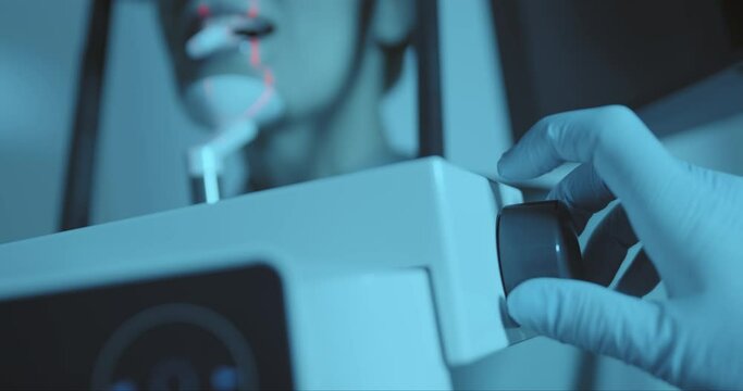 Close up the medical hand in disposable gloves that are rotating a button for properly scanning at the 3D dental tomography (CBCT) while a female patient is standing.
