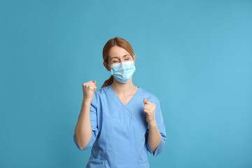 Emotional doctor with protective mask on light blue background. Strong immunity concept