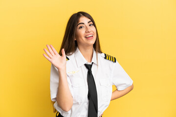 Airplane pilot isolated on yellow background saluting with hand with happy expression